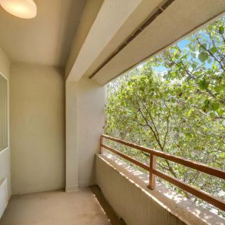 A sunny apartment balcony with a view of leafy trees.