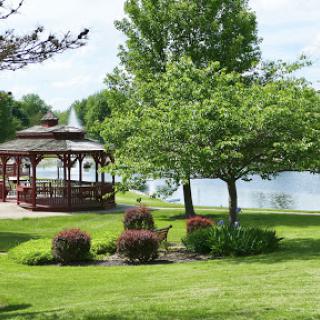 A serene park scene featuring a gazebo beside a tranquil lake, surrounded by lush greenery.
