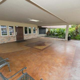 A spacious covered patio with seating and an entrance, surrounded by greenery.