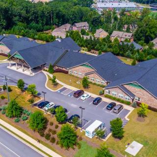 An aerial view of a building complex surrounded by greenery with a parking lot in the foreground.