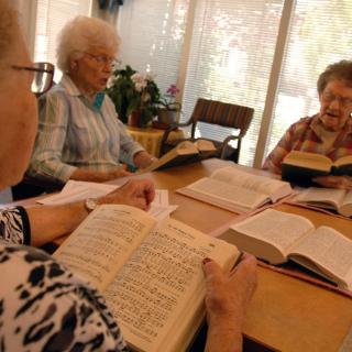 A group of elderly people sitting around a table, reading books together indoors.