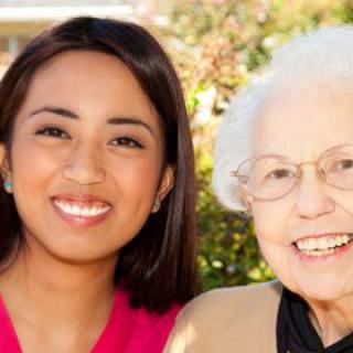 A younger woman and an elderly woman smiling together outdoors.