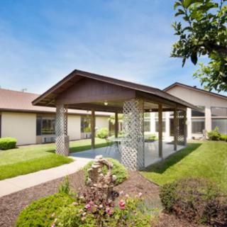 A modern building with a covered walkway and landscaped garden under a clear blue sky.