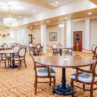 An elegant dining area featuring round tables and upholstered chairs, illuminated by chandeliers.
