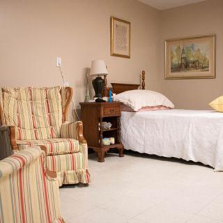 A cozy bedroom with a comfortable bed and armchair, adorned with warm colors and classic decor.