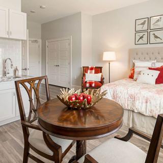 A cozy studio apartment with a kitchenette and a dining area beside a neatly made bed.