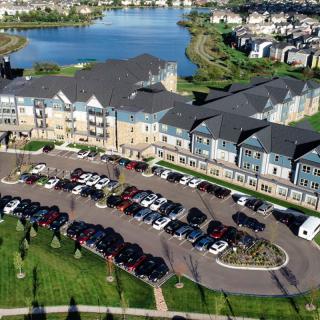 Aerial view of a residential building with a parking lot and nearby lake.