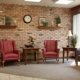 A cozy waiting area featuring red armchairs, wooden furniture, and decorative elements against a brick wall.