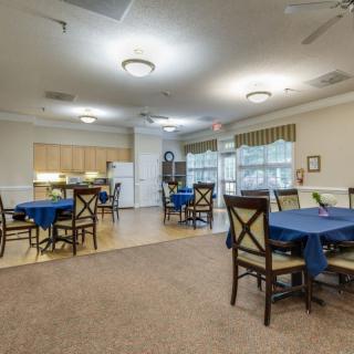 A welcoming dining area with multiple tables and chairs, adjacent to a kitchen in a community setting.