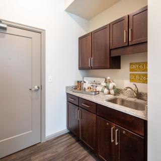 A compact kitchen area featuring dark cabinets, a countertop with a sink, and a door leading to another room.