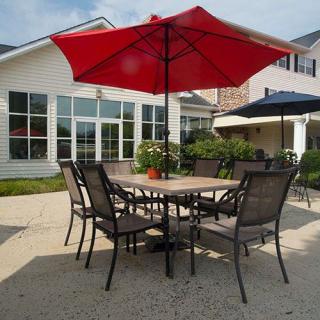 A sunny outdoor patio area with a table, chairs, and a red umbrella.