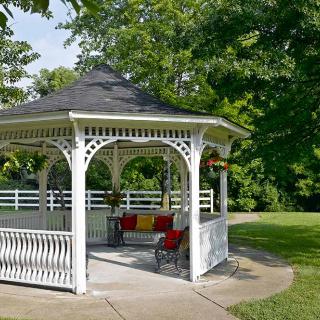 A charming white gazebo surrounded by lush green trees in a tranquil park setting.