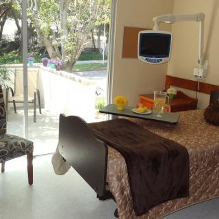 A well-lit hospital room with a bed and a view of the garden outside.