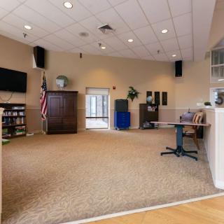 An empty room with carpeted floor, featuring a television, American flag, and various furniture items.