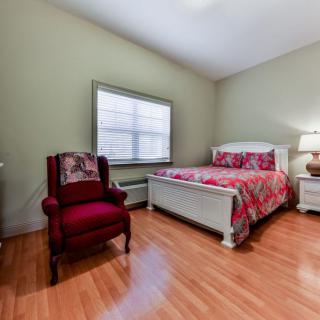 A cozy bedroom with a bed, armchair, and wooden flooring.