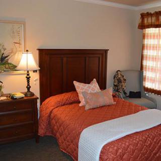 A cozy bedroom with a neatly made bed, wooden headboard, and a nightstand with a lamp.