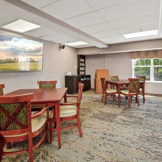 A spacious conference room with several tables and chairs, featuring artwork on the walls and a cozy carpet.