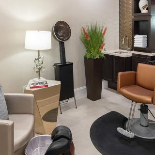 A cozy hair salon interior with seating, a lamp, and hairstyling equipment.