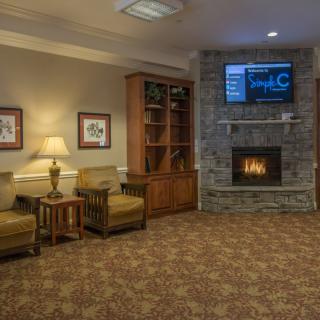 Cozy living room with a fireplace and television, featuring armchairs, a bookshelf, and framed pictures.