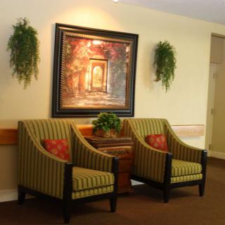 A cozy lobby area featuring two striped armchairs, a framed painting, and decorative plants.