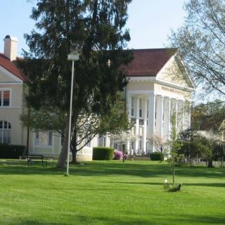 A beautiful historical building with prominent columns surrounded by lush green lawns and trees.
