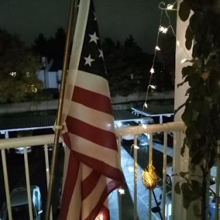 A United States flag gently waving on a balcony, illuminated by soft lights in the night.