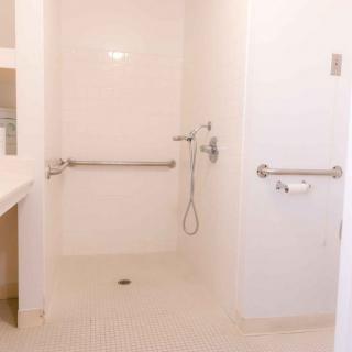 An accessible bathroom featuring a shower area with grab bars and a handheld shower head.