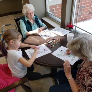 A young girl and two elderly women are engaging in a coloring activity together indoors.
