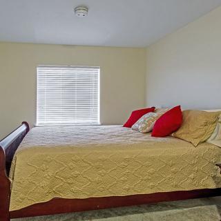 A minimalist bedroom with a large bed, red and beige pillows, and a window with blinds.