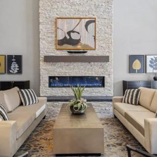 A modern living room featuring two beige sofas, a central coffee table, an elegant fireplace, and abstract artwork on the walls.