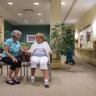 Two elderly women sitting and conversing in a nursing home common area.