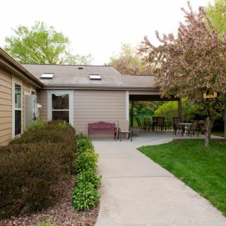A cozy patio area with a pathway leading to a house, surrounded by greenery and well-maintained landscaping.