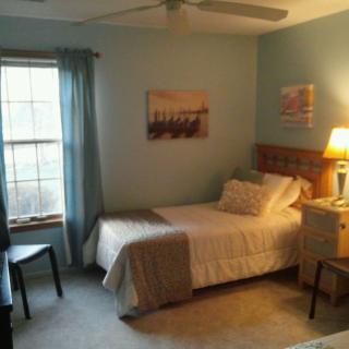 A cozy bedroom with a single bed, side table with a lamp, and a window with curtains.