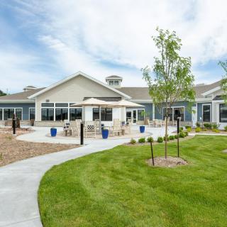 A modern building with a landscaped outdoor area featuring a lawn, trees, and a pathway.