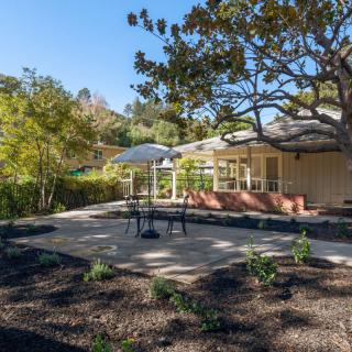 A tranquil patio area with outdoor seating surrounded by a lush garden and trees.