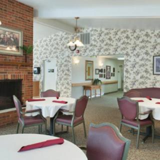 A cozy dining area with tables, chairs, and a brick fireplace, featuring traditional wallpaper and decor.
