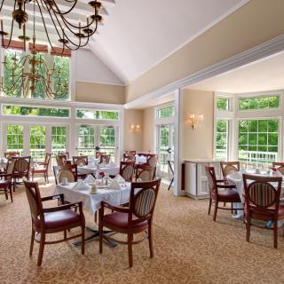 A bright and inviting dining room with elegant chandeliers, large windows, and neatly arranged tables and chairs.
