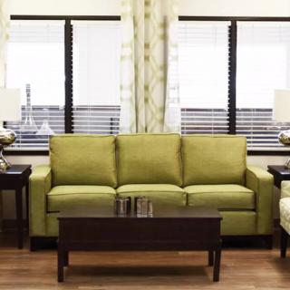 A modern living room featuring a green sofa, dark coffee table, and stylish lamps placed next to large windows.