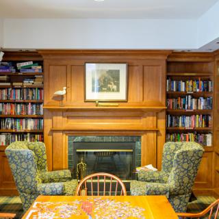 A cozy library room featuring a wooden bookshelf and a fireplace, flanked by two patterned armchairs.