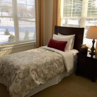 A cozy bedroom with a single bed next to a large window, featuring elegant decor and warm lighting.