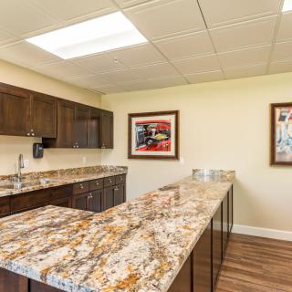 A modern office kitchen with granite countertops and artwork on the walls.