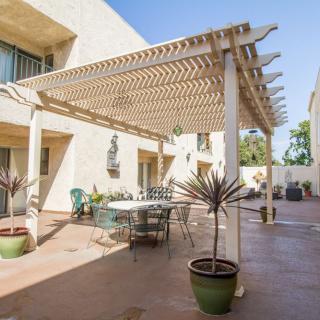 A sunny patio with a pergola, outdoor furniture, and decorative plants.