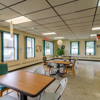 An empty dining area with tables and chairs arranged neatly, lit by natural light from multiple windows.