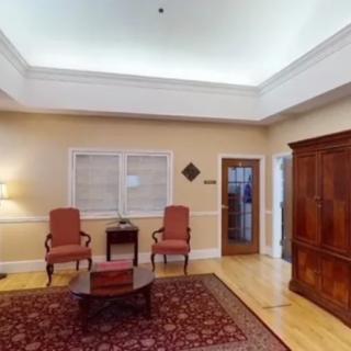 A cozy living room with two upholstered chairs, a wooden coffee table, an armoire, and a patterned rug.