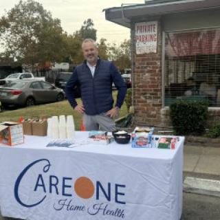 A vendor standing behind a promotional table at an outdoor event.