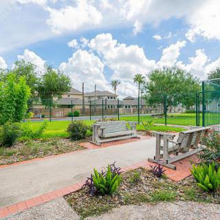 A restful park scene with benches along a pathway, surrounded by trees and greenery under a cloudy sky.