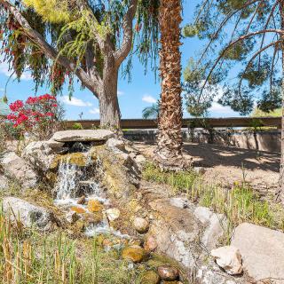 A small garden waterfall surrounded by rocks and trees on a sunny day.