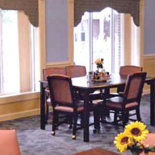 A cozy dining area with a wooden table, surrounded by chairs and decorated with sunflowers near large windows.