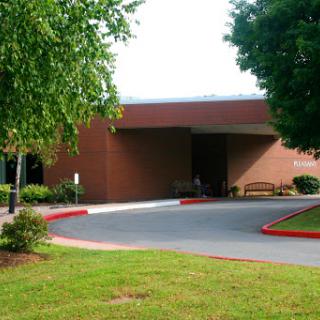 A well-maintained building surrounded by greenery, featuring a clear entrance and parking area.