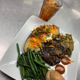 A delicious dinner featuring steak, green beans, a loaded baked potato with sour cream and cheddar cheese, accompanied by iced tea.